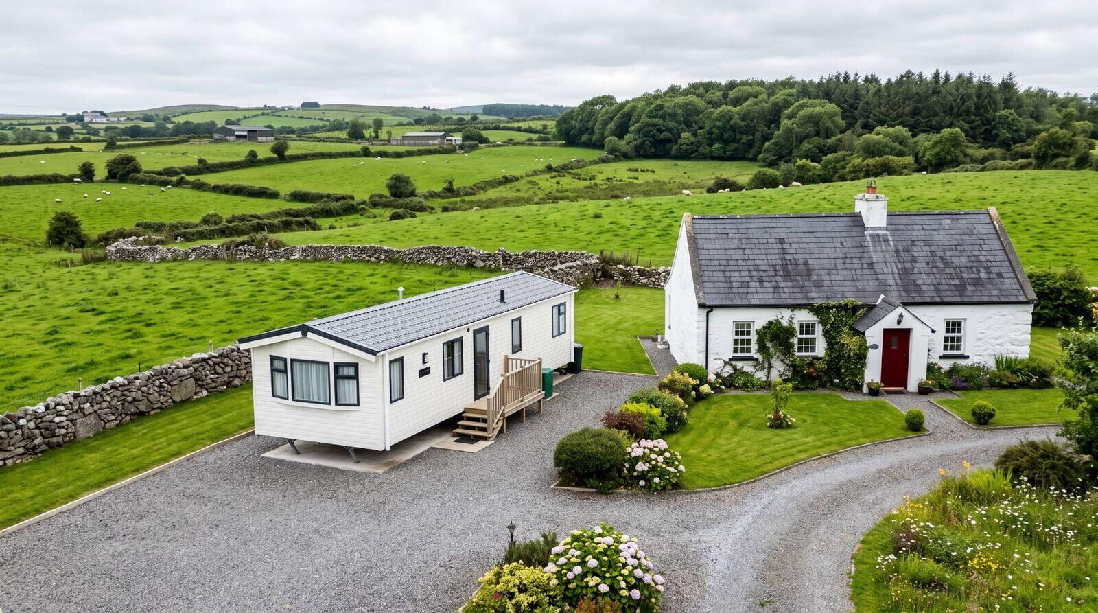 A white mobile home sited on a gravel base beside a rural Irish cottage